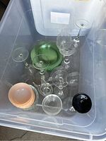 Top view of large plastic bin containing clear stemmed wine and cocktail glasses, green glass plate, small peach-colored bowls, and a black shallow bowl.