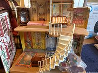 Dollhouse interior shot showing detailed wallpaper, spiral staircase, miniature sofa, cabinet, lamp, table and chairs.