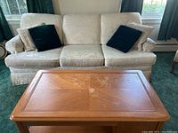 Front view of the off-white floral patterned three-seater couch with four throw pillows and the wooden coffee table in front.