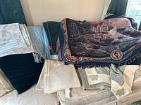 Throw blankets stacked on couch, showing different materials and designs.