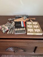 Full view of charcuterie and cheese serving items laid out on a wooden dresser including cutting board with slicer, boxed mini forks, ceramic cheese markers, and loose forks and spreaders.