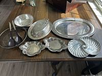Full view of all silver-plated serving dishes and wooden bowl with utensils on table showing all items in the lot