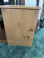 Side view of one wooden side table showing closed cabinet door with round wooden knob, light wood with visible grain and knots