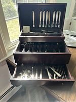 Full view of the Reed & Barton silver-plated flatware and serving utensils in the wooden chest with three drawers open.