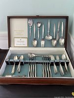 Full case view with all silver-plated utensils displayed neatly in velvet compartments inside a wooden box with hinged lid and Reed & Barton branding on the upper lining.