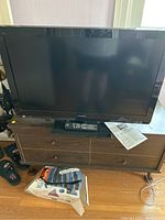 Front view of Panasonic black flat-screen TV on wood console with remote and manual in front.