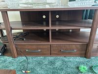 Front view of wood TV stand showing open shelves with cable holes and two lower drawers with metal handles.
