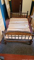 View of the assembled antique spool bed frame showing the wooden slat base and headboard and footboard with spindle design
