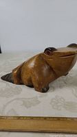 Front angled view of the carved wooden frog on a fabric surface with a ruler to show size, approximately 10 inches long.
