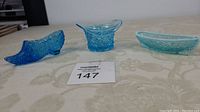 Three blue glass collectible pieces on table: shoe figurine, top hat, and canoe dish as seen from a distance.
