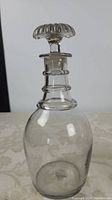 Front view of clear glass decanter showing rounded body and three ring neck with scalloped stopper.