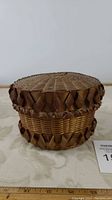 Front angled view of small round hand woven basket showing decorative brown woven border and woven texture