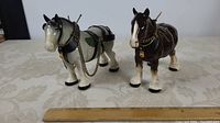 Pair of porcelain Shire Clydesdale draft horse figurines on a table with a ruler showing scale.
