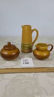 Three pieces together on table: mustard yellow pottery pitcher with handle and green swirl decoration, Myott Ironstone lidded jar, and small Myott Ironstone pitcher.