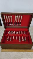 Wooden chest open displaying full cutlery set with red felt interior.