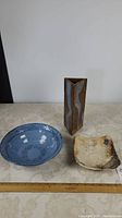 Overall photo of all three pottery pieces: triangular vase, fruit bowl, and footed tray