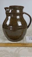 Side view of the brown speckled pottery pitcher with a ruler showing an 8 inch height.