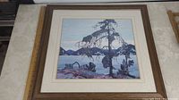 Full view of the framed art print of The Jack Pine by Tom Thomson showing the wooden frame, cream matting, and central tree image with background lake and mountains.
