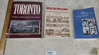 Three Toronto-related books placed side by side on a beige patterned surface.