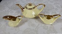 Pearl yellow china tea set consisting of teapot, creamer, and sugar bowl with gold trim