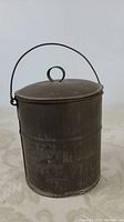 Side view of oval-shaped vintage tin lunch pail showing patina and wire handle.