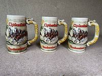 Set of three matching vintage ceramic beer mugs showing front and handles with embossed Clydesdales and Budweiser branding.