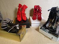Four pairs of women's fancy high heeled shoes in their original boxes: two pairs are red, two pairs are black with various strap and lace-up details.