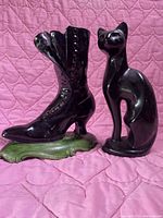 Front view of black ceramic Victorian shoe and cat figurines against pink quilted fabric.