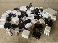 Photo showing multiple black and white cellphone chargers with attached cables and power adapters spread on surface.