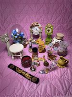 Photo showing diverse group of decorative figures, clocks, glass and ceramic items arranged on a pink quilted surface