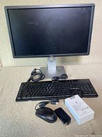 Front view of Dell monitor on adjustable stand with black keyboard, wired mouse, and power adapter on surface.