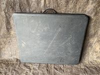 Closed black folding table showing surface wear and scratches, with rounded edges.