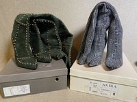 Two pairs of high knee boots placed on their respective boxes, showing dark green suede with studs and black houndstooth patterned boots.