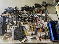 Overview of assorted tools on table showing hammers, clamps, pliers, battery chargers, and hand planes.