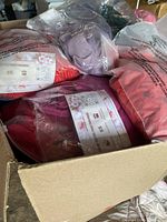 Box filled with assorted packaged clothing items in plastic bags including various colors and designs.