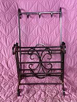 Folded iron cast firewood rack showing horizontal and vertical bars with scrollwork design.