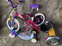 Photo showing two kids bikes and one kids scooter placed on a cloth background