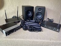 Front view of lot showing USB audio interface, two black bookshelf speakers, five wireless microphones, and two wireless receiver units with antennas.