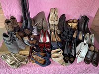 Wide view of all 21 shoes arranged on pink quilted surface, showing various styles from boots to heels and slip-ons.