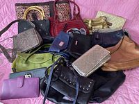 Overview of all 15 various handbags and wallets arranged on pink textile, showing different textures and colors.