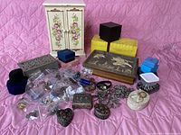 Overview of jewelry, decorative boxes, and jewelry cabinet in front of pink quilted background