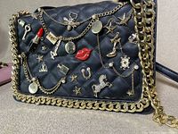 Close-up of black purse with various gold-tone decorative charms and chains attached to quilted surface.