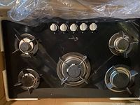 Top-down image showing the entire 5-burner gas cooktop with black glass surface and metal knobs.