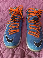 Front view of blue Nike LeBron XII Elite Elevate shoes with orange laces and black Nike swoosh.