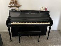 Front view of black upright piano with storage bench in front.