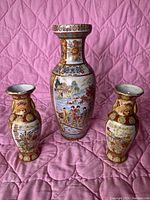 Full view of all three Chinese pottery vases on pink quilted fabric with varied sizes and detailed moriage decoration.