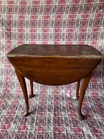 Side view of the vintage wooden drop leaf side table with folded leaves, showing curved cabriole legs and dark brown finish.
