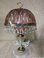 Front view of pink crystal domed boudoir lamp showing carved glass shade, decorative metal rim, and clear crystal prisms hanging from edge, with clear glass and brass base.