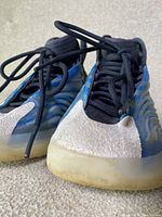 Pair of Yeezy sneakers showing toe area with grey suede and black laces, blue side panel, and translucent sole slightly yellowed.