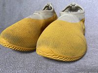 Close-up front view of Yeezy shoes showing knit yellow and beige upper and rubber sole with slight dirt visible.